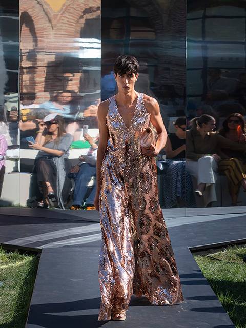 Una modelo camina por la pasarela mientras la audiencia observa atentamente en un evento de moda.