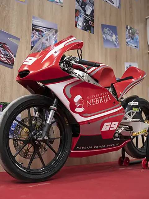 Una moto de carreras de color rojo con el logo de la Universidad Nebrija exhibida en un evento.