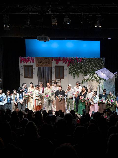 Un grupo de actores en el escenario al final de una representación teatral, recibiendo aplausos del público.