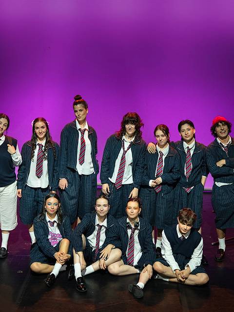 Un grupo de jóvenes en un escenario, vestidos con uniformes escolares, posando para la foto.