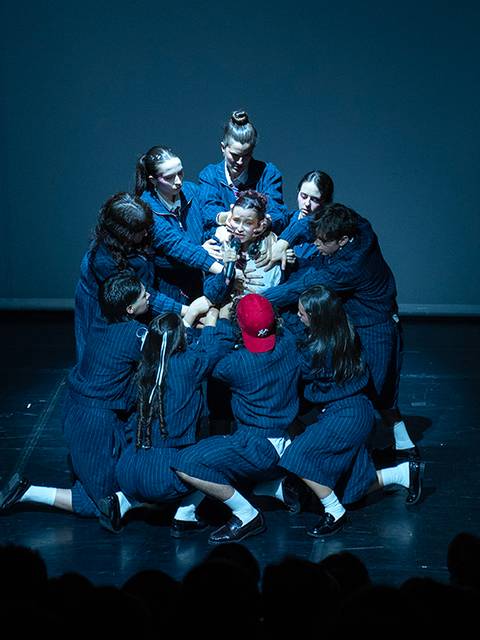 Un grupo de personas en un escenario están rodeando y sosteniendo a una figura central en una representación teatral.