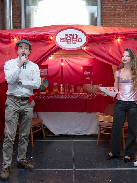 Un evento con una presentación en un escenario decorado, donde un hombre habla mientras dos mujeres lo escuchan en un ambiente festivo.