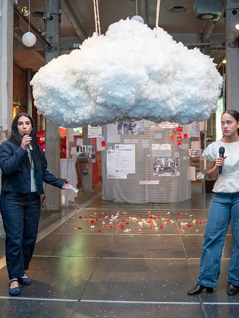Una instalación artística con una nube de material suave colgando en un espacio mientras cuatro personas interactúan en su interior.