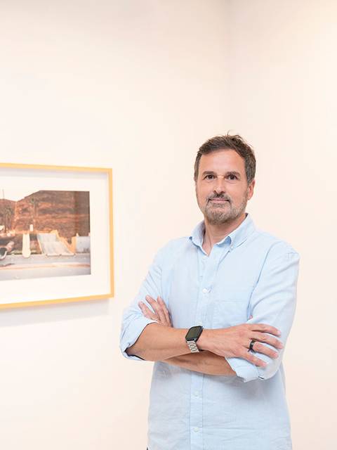 Un hombre posando en una galería de arte frente a varias fotografías enmarcadas.
