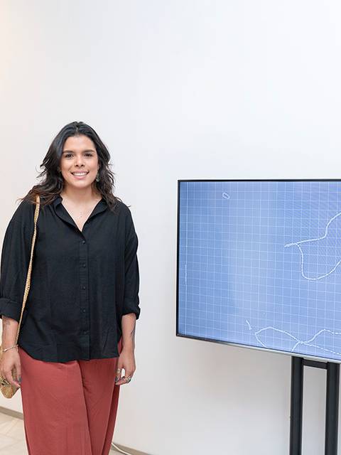 Una mujer sonriente está de pie junto a una pantalla en una galería de arte.