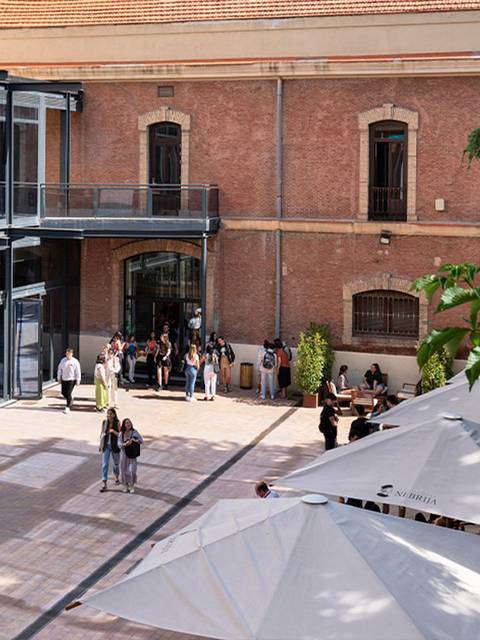 Una plaza con personas y sombrillas en un ambiente arquitectónico moderno y acogedor.