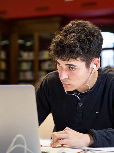 Un joven concentrado trabajando en un ordenador portátil en un ambiente de estudio.