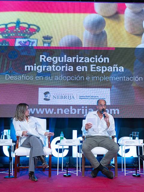 Un panel de discusión sobre la regularización migratoria en España con varios ponentes en un evento.