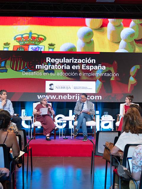 Una conferencia sobre la regularización migratoria en España con varias personas sentadas en un panel discutiendo el tema.