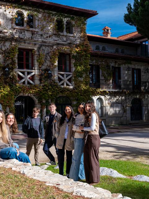 Grupo de personas posando frente a un edificio antiguo con vegetación.