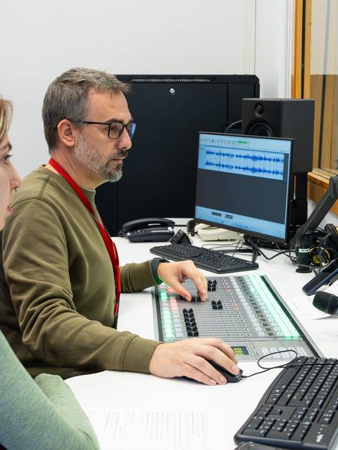 Dos personas trabajan en un estudio de sonido, una de ellas operando un equipo de mezcla.