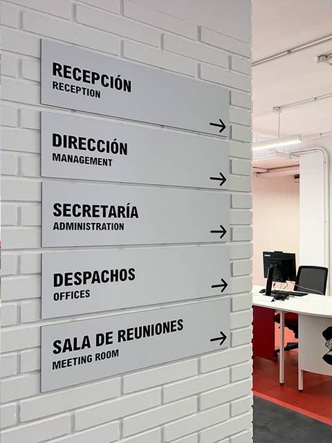 Una vista interior del Instituto Nebrija con señalización de diferentes áreas y una recepción.