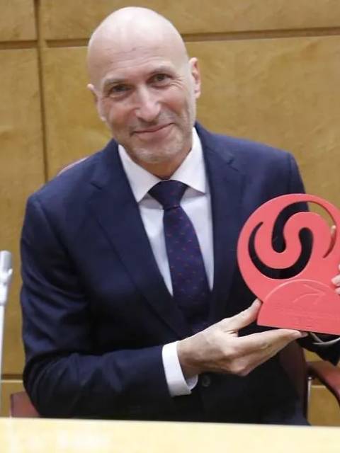 El hombre sonriente sostiene un trofeo en un entorno formal.