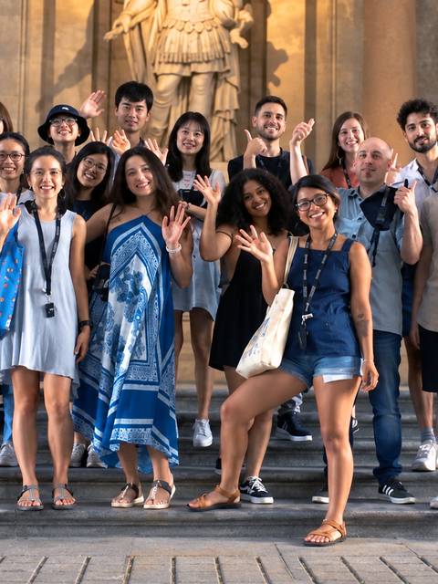 Grupo de personas posando y sonriendo frente a una estatua en un edificio histórico.