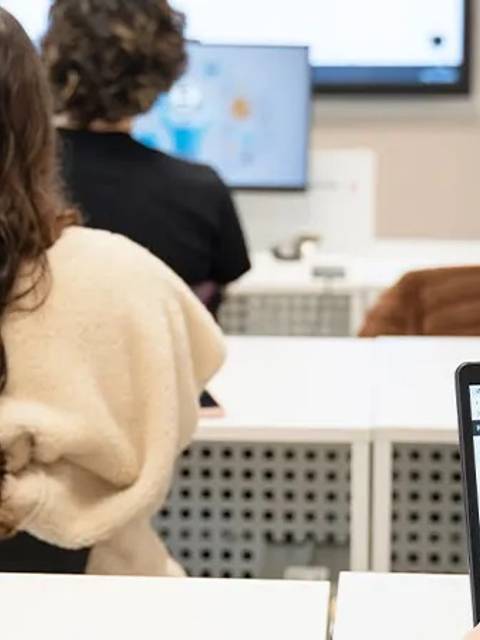 Un grupo de estudiantes sentados en un aula prestando atención a la pantalla.