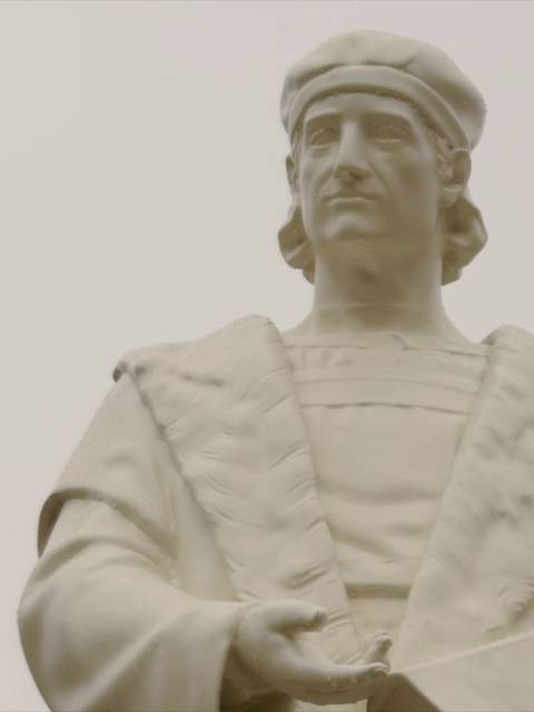 Escultura de un hombre con vestimenta histórica en un fondo nublado.