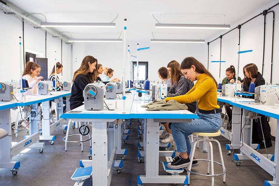Un grupo de mujeres jóvenes trabaja en máquinas de coser en un taller de costura.