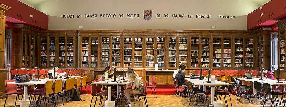 Una biblioteca con estanterías llenas de libros y personas estudiando en mesas.