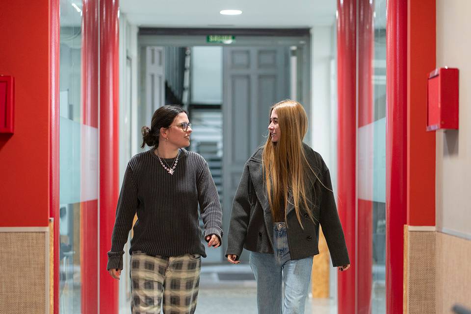 Dos jóvenes caminando y conversando por un pasillo iluminado.