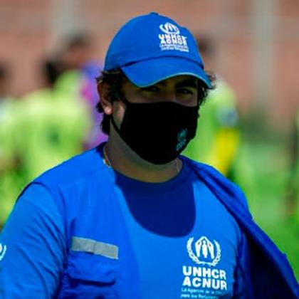 Un hombre con gorra y camiseta azul que representa a ACNUR camina por un campo.