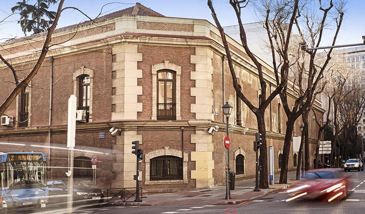 Edificio histórico en una esquina con árboles desnudos y tráfico en la calle.
