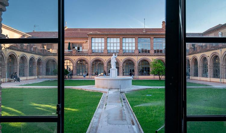 Vista del patio de un edificio con una estatua en el centro y arcos a los lados.