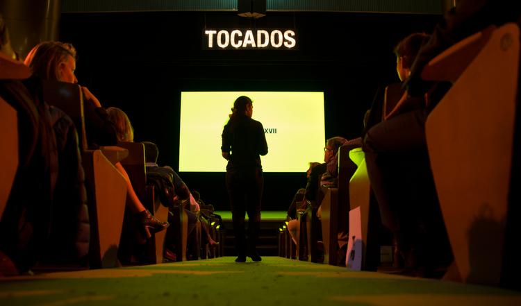 Una persona de pie frente a una pantalla en un evento con el título 'TOCADOS'.