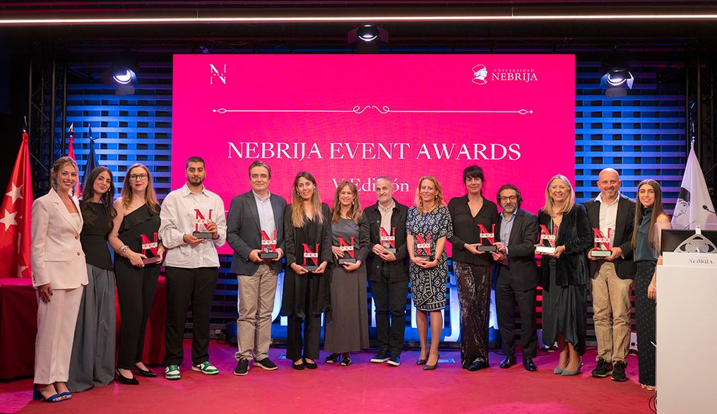 Ceremonia de entrega de los Nebrija Event Awards con un grupo de premiados posando frente a un fondo iluminado en rosa.