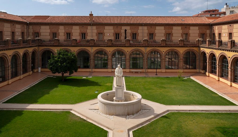 Vista del patio de un edificio con una estatua en el centro y arcos en las paredes.