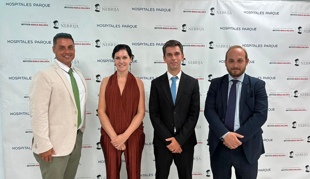 Cuatro personas de pie posando en un evento formal con un fondo de marca.