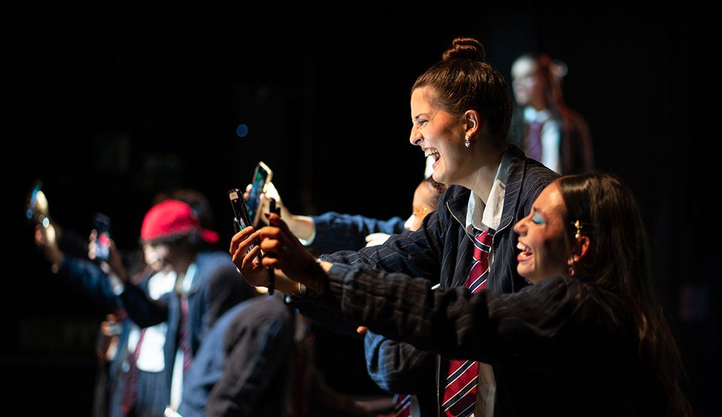 Un grupo de jóvenes sonríe mientras toman selfies en un escenario.