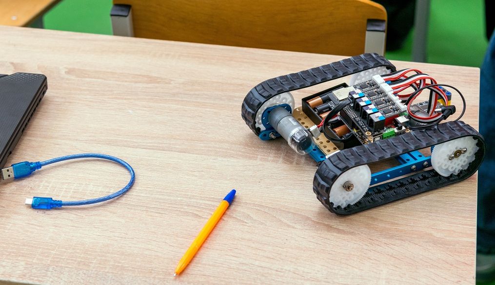 Una mesa con un robot sobre orugas, un lápiz y un cable USB.
