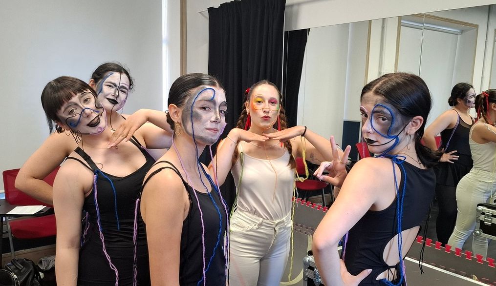 Un grupo de cinco personas posando con maquillaje artístico en un ambiente de vestidor.