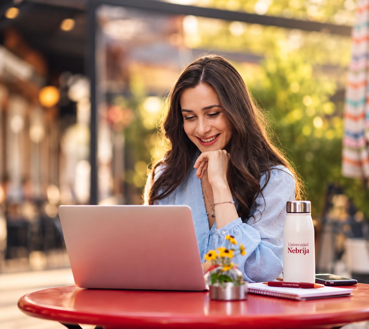 Una mujer sonriente trabaja en su laptop mientras disfruta de un ambiente al aire libre.