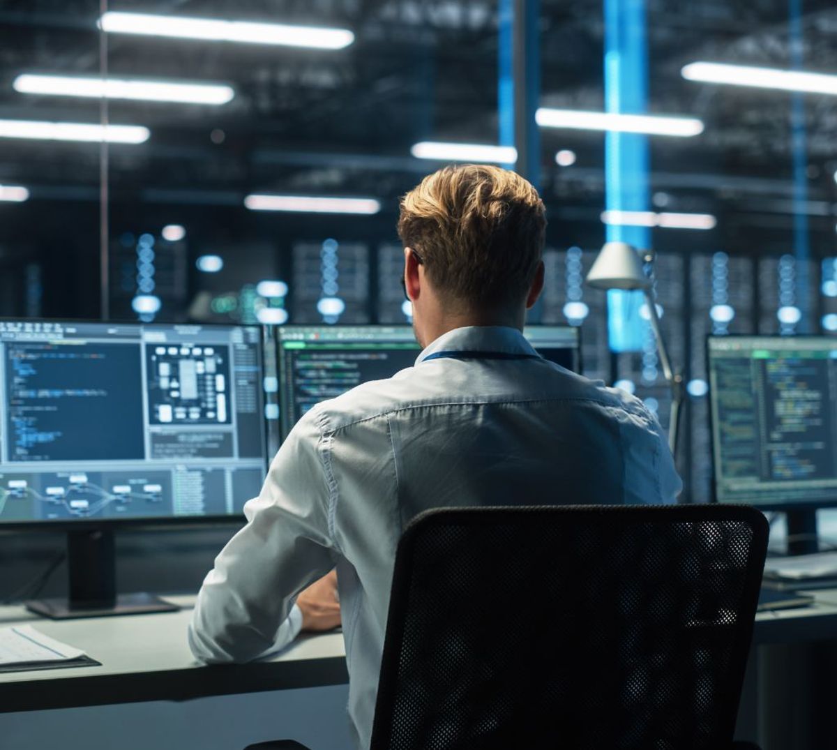 Un hombre sentado frente a múltiples pantallas de computadora en un entorno de oficina moderna.