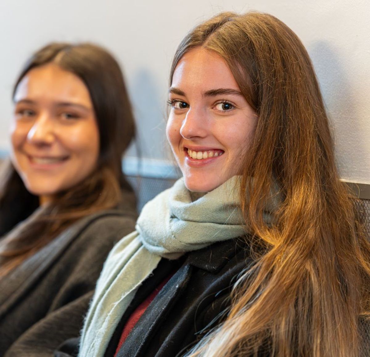 Dos jóvenes sonrientes están sentadas una al lado de la otra en un ambiente interior.