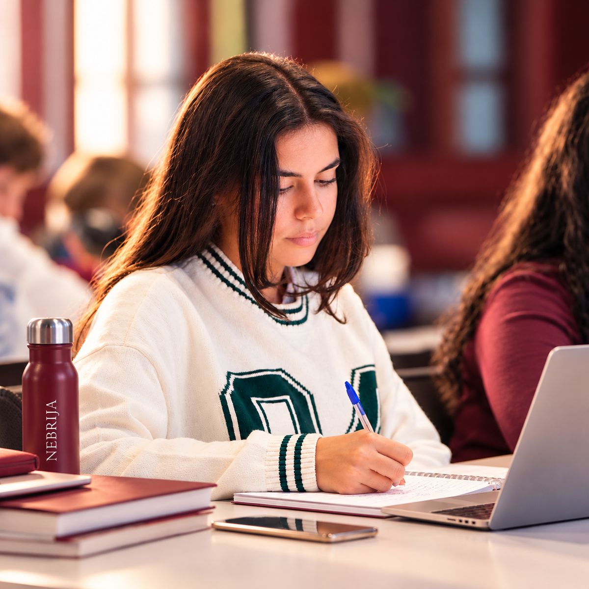 Una estudiante concentrada escribe en su cuaderno mientras se encuentra en un aula.