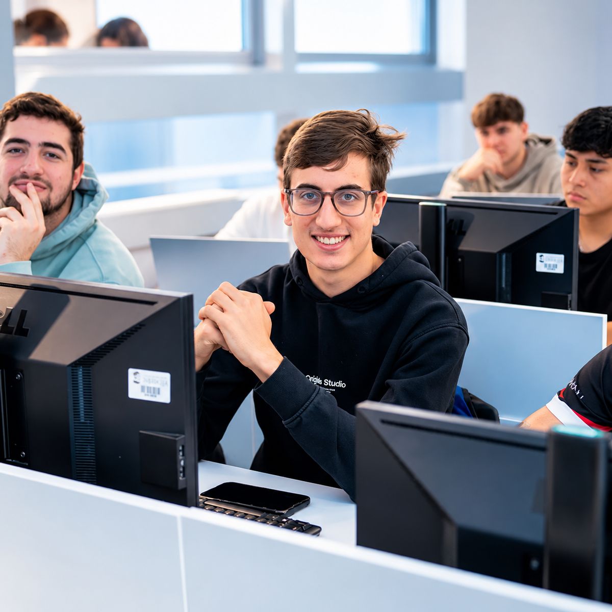 Un grupo de estudiantes sonrientes frente a sus computadoras en un aula moderna.