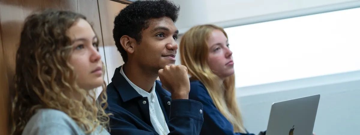 Tres jóvenes atentos durante una clase o presentación.