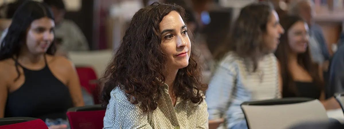 Una mujer con cabello rizado mira con atención en un evento o presentación rodeada de otras personas.