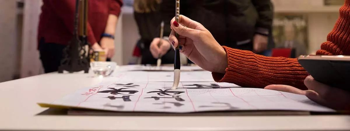 Una persona está practicando caligrafía en una mesa con varias hojas y un pincel.