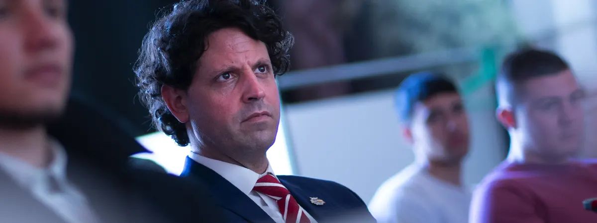 Un grupo de personas escucha atentamente durante un evento, destacando a un hombre de traje con expresión seria.