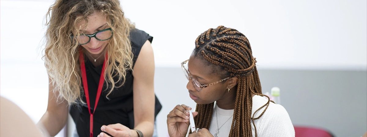 Una mujer con cabello rizado y otra con trenzas están colaborando en una actividad, mostrando interés y concentración.