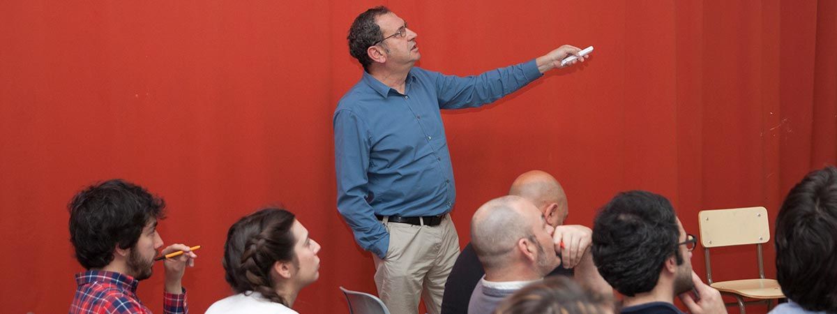 Un hombre de pie señala con un puntero mientras un grupo de personas lo observa en un entorno académico.