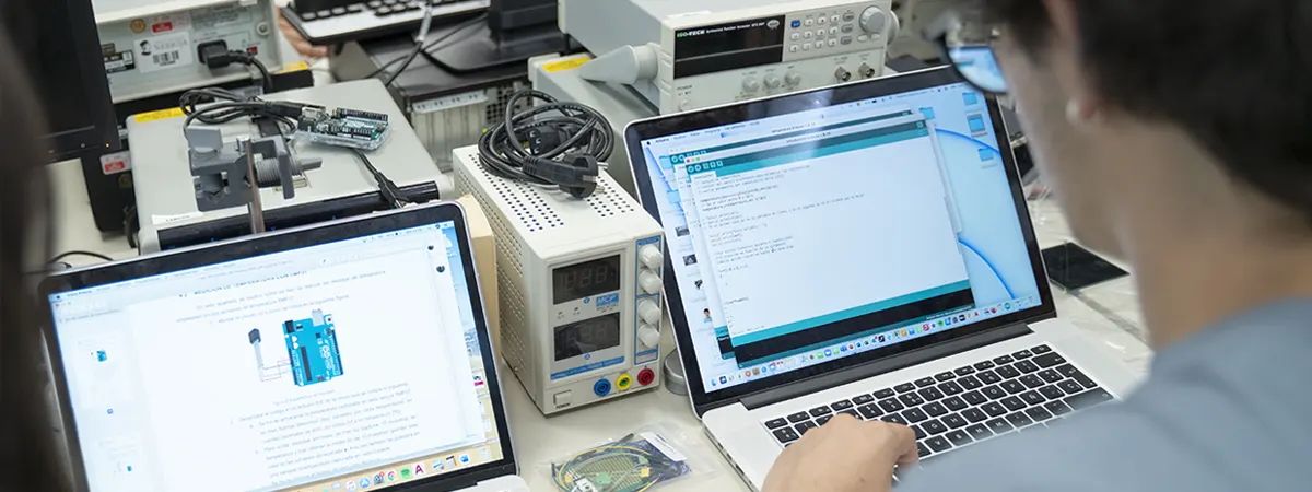 Una persona trabaja en un proyecto tecnológico usando varias computadoras y equipos de laboratorio.