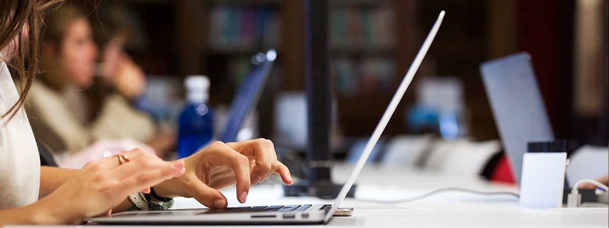 Una persona escribe en una computadora portátil mientras otras personas trabajan al fondo.