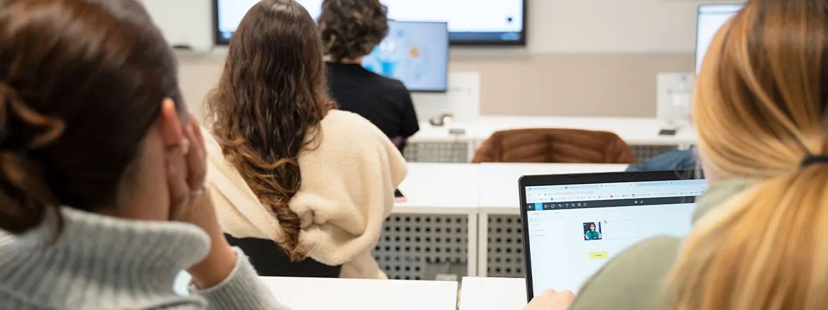Un grupo de estudiantes sentados en un aula prestando atención a la pantalla.
