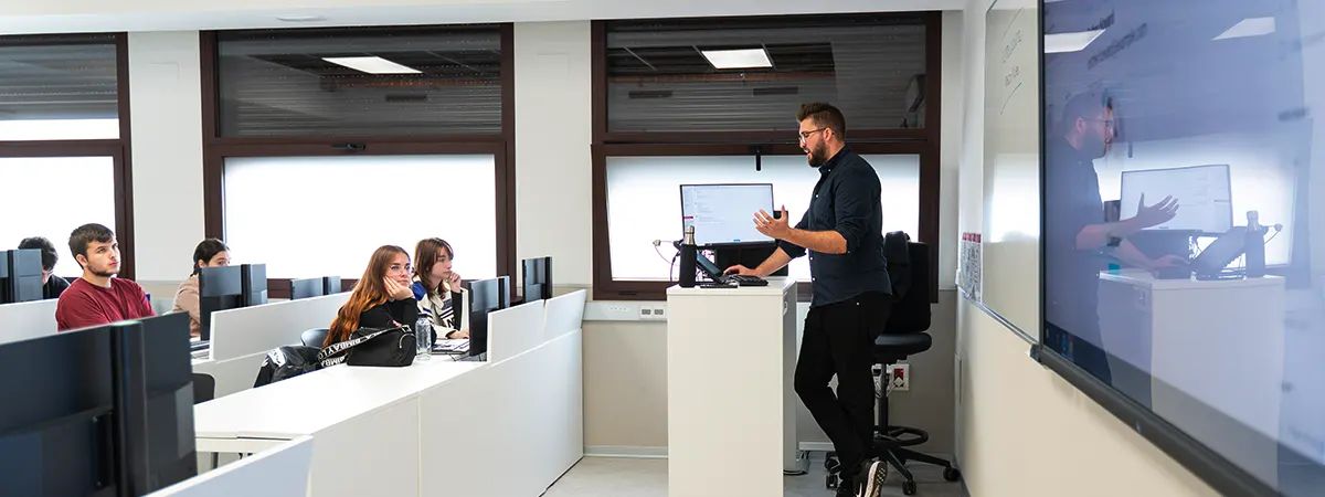 Un maestro presenta un tema a un grupo de estudiantes en un aula moderna y equipada con computadoras.