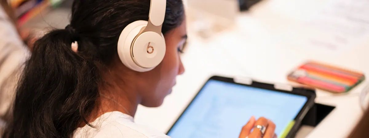 Una persona joven utiliza unos auriculares mientras interactúa con una tableta.