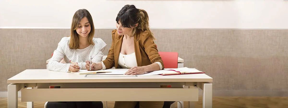 Dos mujeres están trabajando juntas en una mesa, concentradas en una tarea.